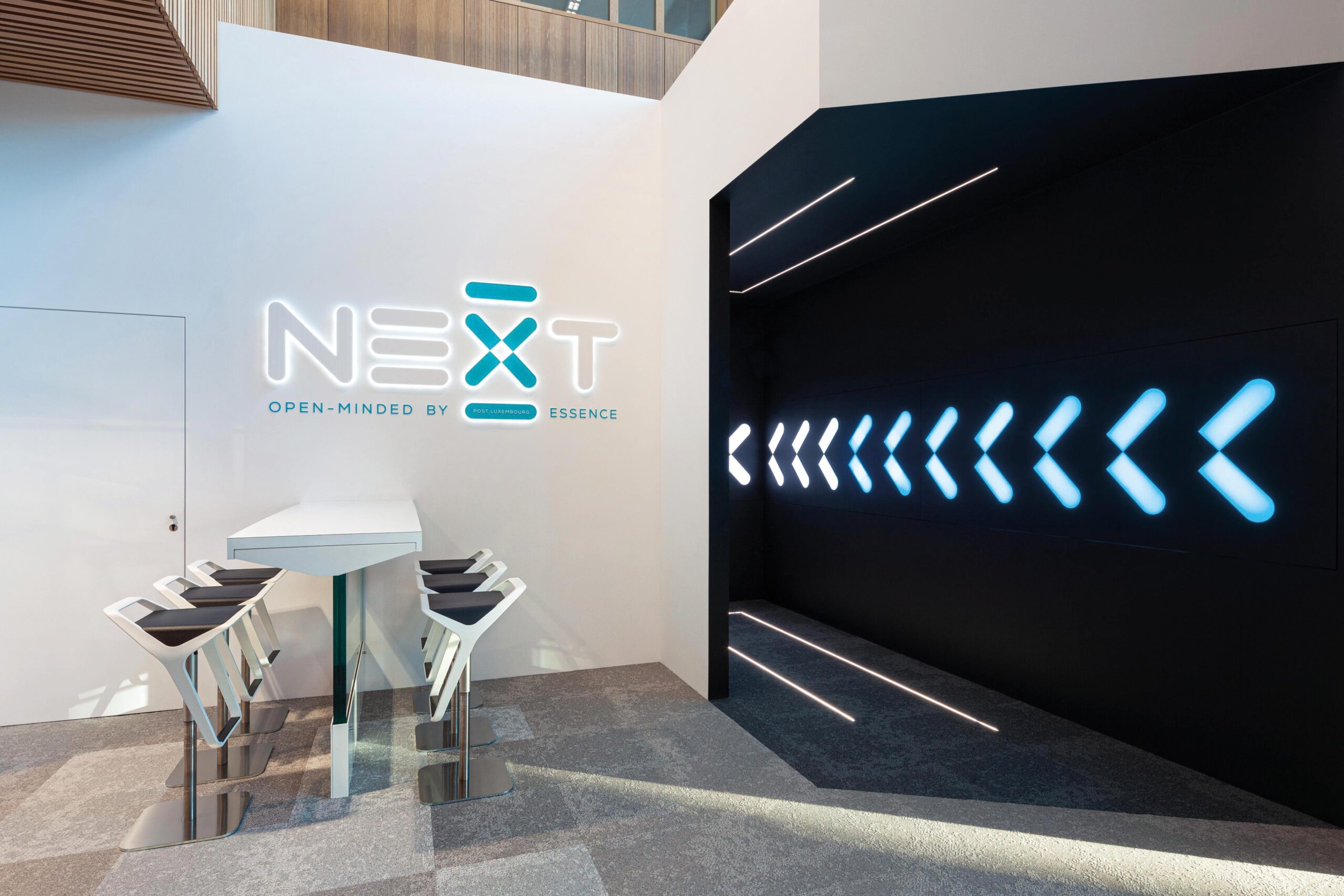 Vue immersive de NEXT, un espace de 400 m² conçu pour inspirer la collaboration et la créativité au sein de POST Luxembourg, avec une scénographie épurée et lumineuse. Design minimaliste dominé par des déclinaisons de blanc, enrichi de textures et de matières variées, réchauffé par des touches de bois aux teintes naturelles.